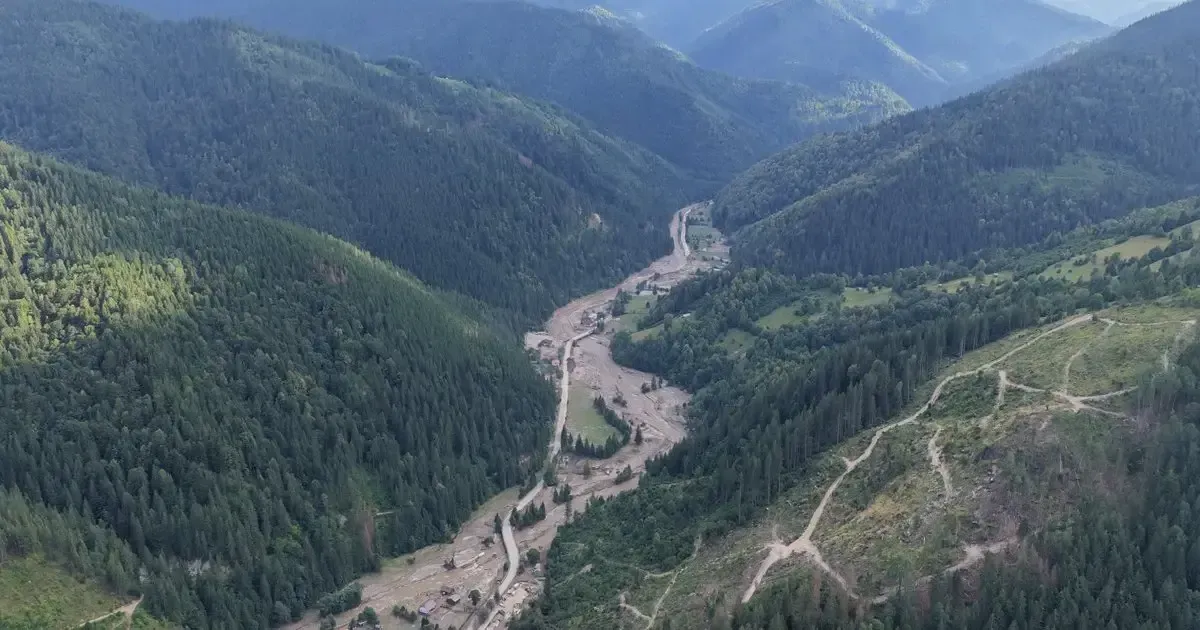 Valea Negrei văzută din dronă după viitură: albia lărgită și acoperită de aluviuni, între versanți împăduriți, cu drumuri de scos-apropiat pe panta din dreapta