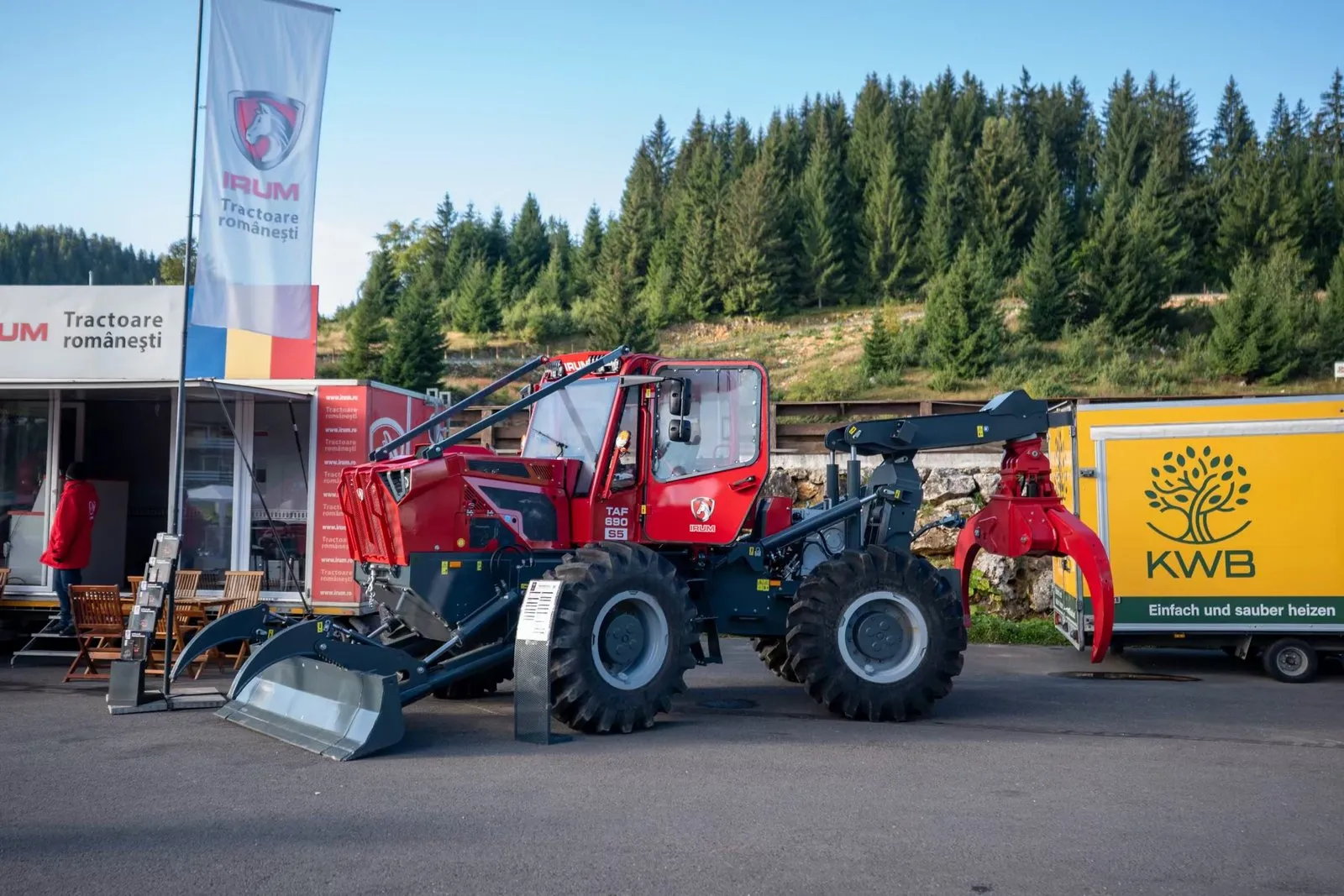 Tractor forestier românesc IRUM, roșu, expus la un târg în aer liber, cu pădure de molid în fundal