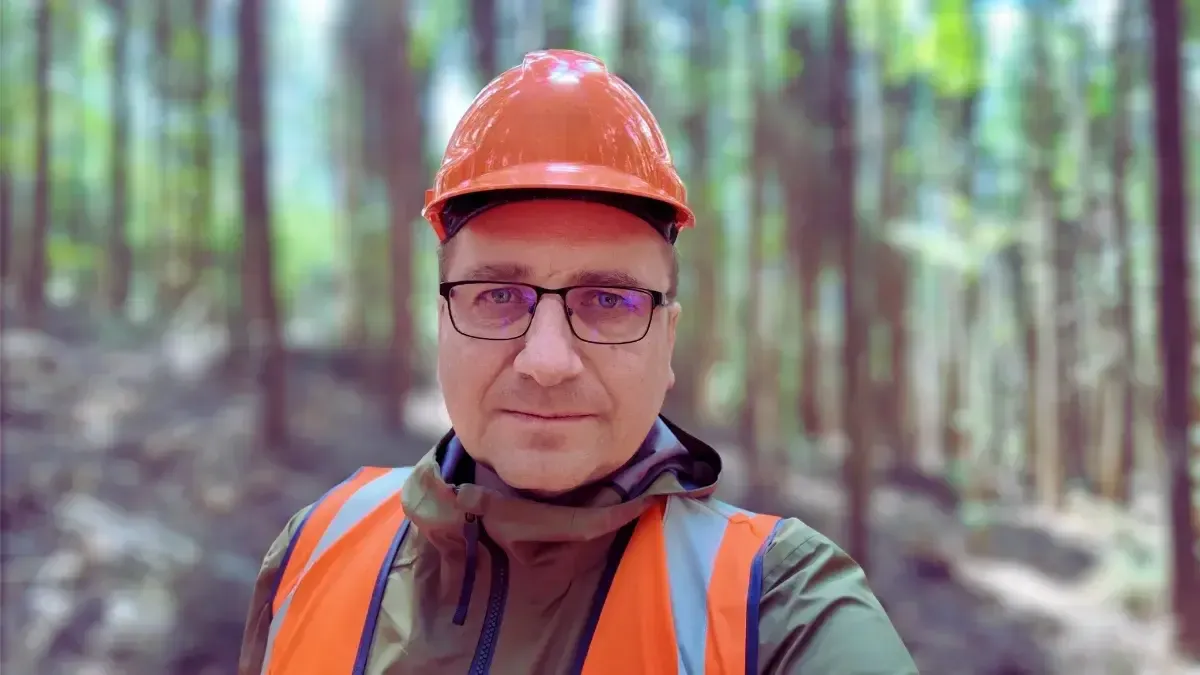 Ciprian Dumitru Muscă cu cască de protecție portocalie și vestă reflectorizantă, în pădure