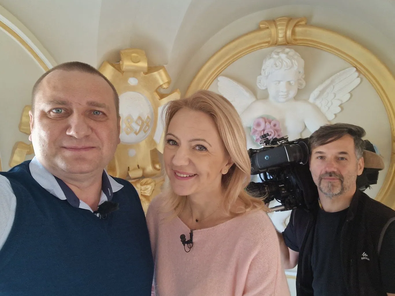 Ciprian Dumitru Muscă, o jurnalistă și un operator cu camera de filmat, fotografiați în fața medalionului cu înger restaurat și a cartușului aurit cu anul 1898