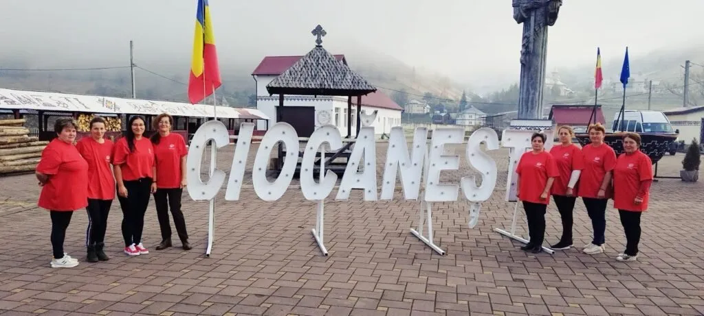 Grup de femei în tricouri roșii în fața literelor mari „Ciocănești”, într-o piață cu steaguri