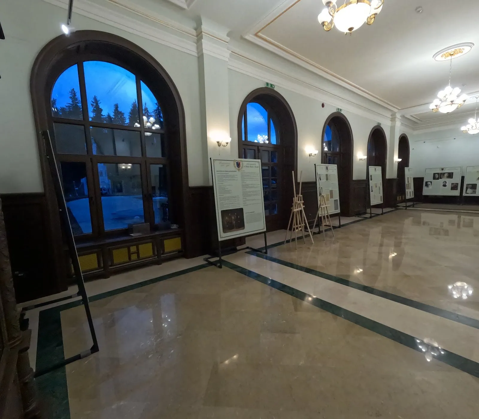 Salon de expoziție cu pardoseală de marmură lucioasă, ferestre mari în arc și panouri expoziționale pe pereți