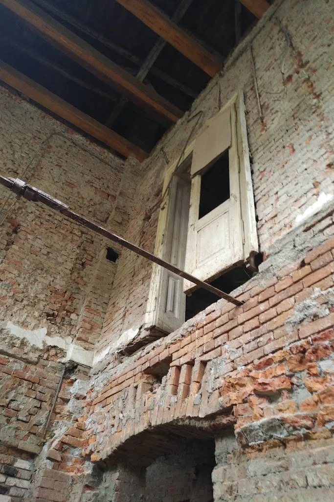 Perete interior de cărămidă dezvelită, cu o ușă de lemn suspendată la înălțime și grinzi de lemn deasupra